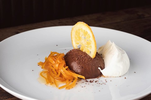 Chocolate mousse dessert with candied orange peel, dried orange slice, and cream on a white plate