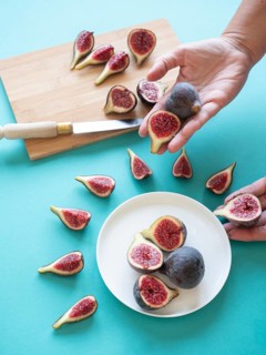 Hands arranging fresh, cut figs on a white plate and cutting board