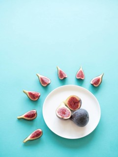 Figs, whole and sliced, arranged on a plate and around on a light blue background