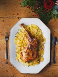 Roasted leg of lamb serving with sliced potatoes and fresh thyme on a wooden table