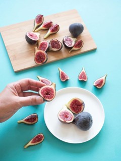 Hand holding fresh cut fig over a plate with more figs