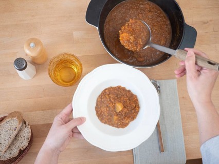 Hands serving lentil soup with potatoes in a white plate on a wooden table, healthy eating concept
