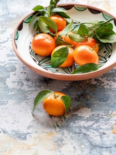 Vibrant tangerines with green leaves arranged in a decorative ceramic bowl, creating a rustic and