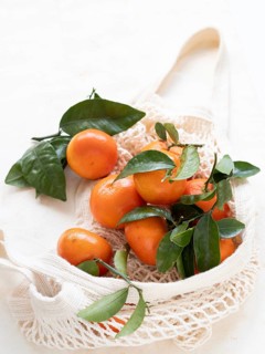 Vibrant tangerines with green leaves are nestled in a reusable shopping bag, promoting a