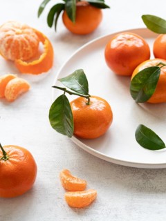 Vibrant tangerines with green leaves, showcasing freshness and citrusy appeal on a white plate and