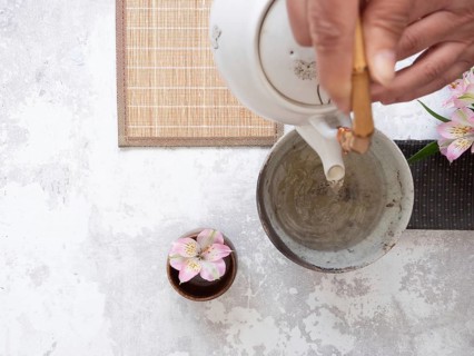 Hands gracefully pouring tea from a white teapot into a ceramic bowl, embodying the tranquility and