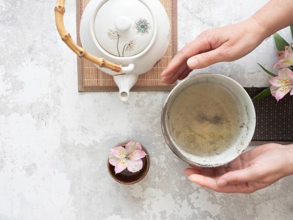 Woman gently holding a tea bowl during a traditional japanese tea ceremony, with teapot and flower
