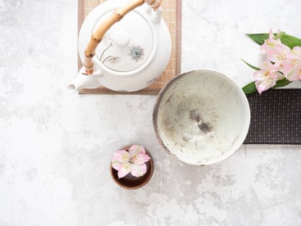 Asian tea ceremony arrangement with white teapot, empty bowl, pink flowers and bamboo placemat on