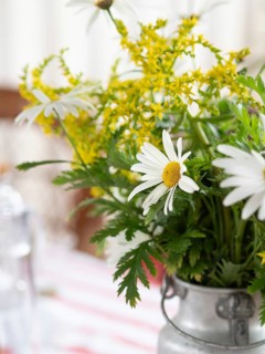 White daisies and yellow wildflowers create a cheerful centerpiece in a rustic metal vase on a