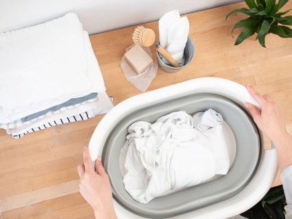 Woman soaking white laundry in a collapsible basin using natural soap, promoting sustainable and