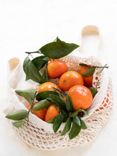 Ripe tangerines with green leaves inside a reusable mesh bag promoting sustainable shopping