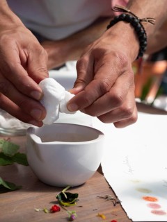 Hands squeezing white flower petals above a mortar for creating natural inks and pigments in a