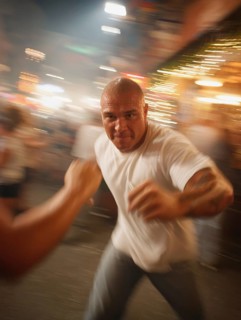 A man gets into a fighting stance, surrounded by dynamic movement and a background filled with