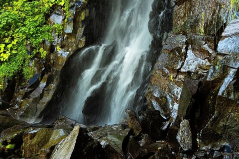 Vaucoux waterfall cascades gracefully over dark rocks, surrounded by lush greenery, Auvergne
