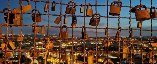 Metal grid full of love locks against an illuminated city backdrop in the evening, view of Lisbon