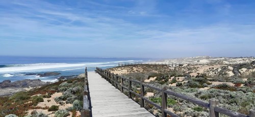 A wooden footbridge leads through vegetation along the coast, hiking on the Fisherman's Trail,