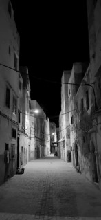 Black and white shot of a dark alley in Essaouira with sparse lighting and historic buildings,