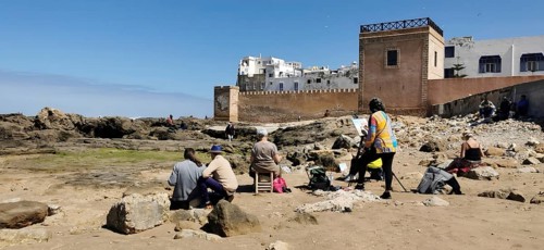 People sitting with canvas on the rocky beach of Essaouira the city view in front of the city wall