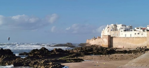 View of coastal landscape with city walls of Essaouira, waves and a small sandy beach with big