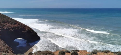 A picturesque coastline with a natural rock arch and strong waves in the blue ocean near Sidi Ifni,