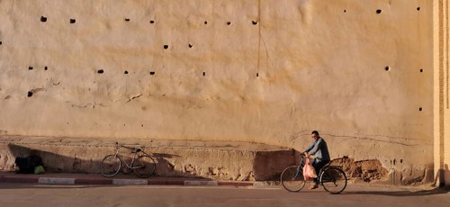 An old city wall with a cyclist riding along in the shade, Taroudannt, Morocco