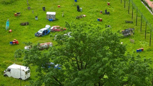 Green field with scattered car wrecks and barrels surrounded by trees, Poland