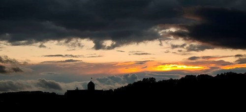 A dramatic sunset with dark clouds over a hilly landscape