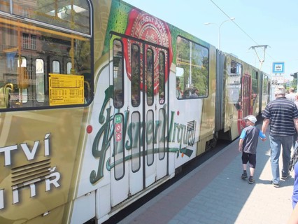 A tram with an advertising message from Pilsner Urquell passes a bus stop, Pilsen, Czech Republic