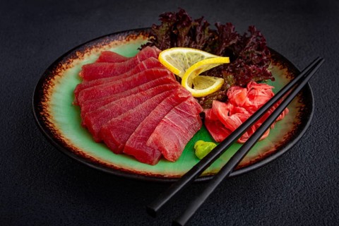 Fresh tuna sashimi served with lemon, wasabi, and pickled ginger on a dark background