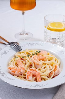 Pasta with shrimp and thyme, served on a white plate, with a glass of white wine, the table is set,