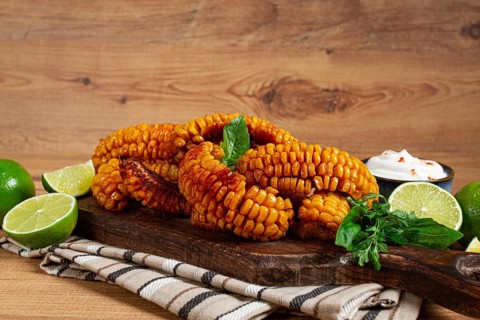 Corn ribs, with cream sauce, spices and lime, appetizer, on a wooden cutting board, homemade, no