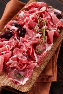 Freshly cut dried meat, served with olives and herbs, on a wooden chopping board, no people
