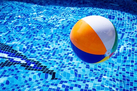 Colorful beach ball floats on the surface of a pool reflecting sunlight on a summer day