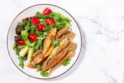 Fried crispy mullet fish, with fresh salad, on a plate with lime, no people