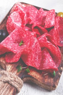 Sliced salami sausage, on a wooden chopping board, decorated with olives and herbs, close-up, no