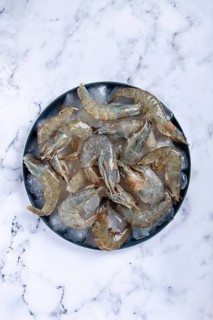 Fresh raw shrimp, spread on ice with lemon and cilantro slices on a marble surface, ready to cook,