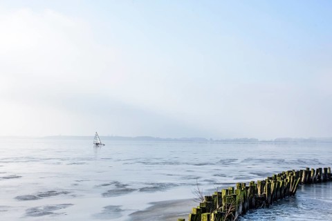 Ice sailor on frozen Dümmer Lake, shore with wooden structures, Lembruch, Lower Saxony, Germany