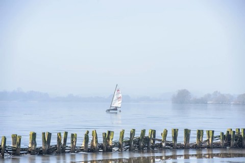 Ice sailor sails on a lake with wooden barriers in the foreground, blue sky, cold winter day on