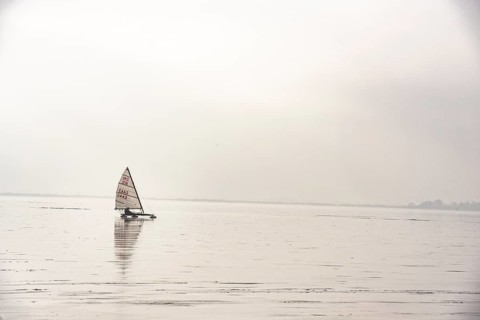 Ice sailor glides across a foggy, frozen lake, quiet winter landscape on frozen Dümmer Lake,