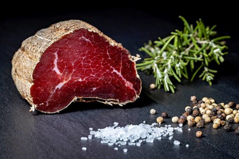 Delicate sausage piece on slate plate with salt and peppercorns, delicatess ham fresh from the