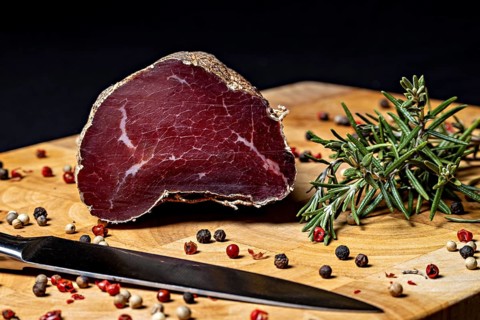 Delicatesswurst on wooden board decorated with peppercorns and rosemary, delicatess ham fresh from