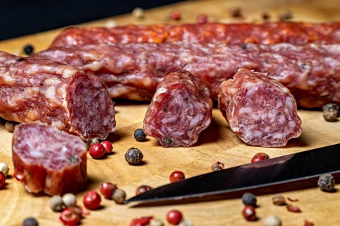 Close-up of salami slices with peppercorns and a knife on wood, crunchy pepperbeiser sausage
