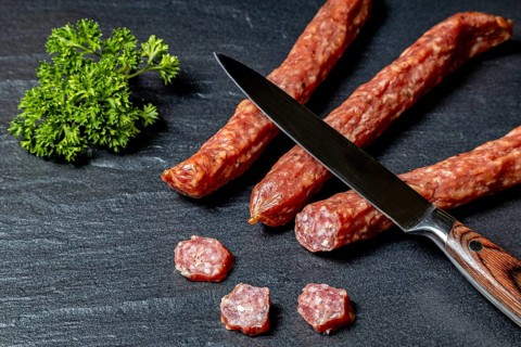 Salami with cutting knife and parsley on a dark surface, crispy pepper sausage