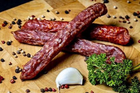 Salami on wooden board decorated with spices and garlic clove, crunchy pepper bite sausage