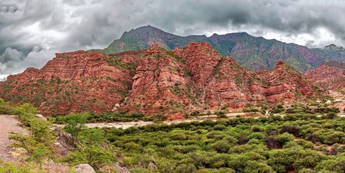 Red rock formations rise against green vegetation and cloudy skies, the landscape and colorful rock