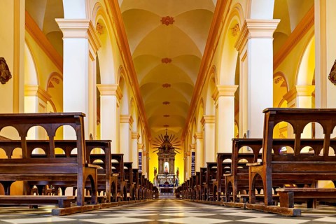 View along the aisle in a church interior with rows of seats, magnificent columns and an altar, the