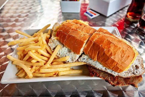 Large sandwich with fries served on a metal table, thickly filled with bread and a fried egg