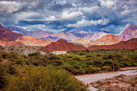 River flows through green vegetation against a mountain backdrop with red hills, the landscape and