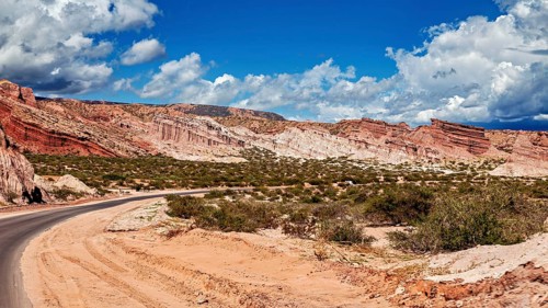 Road snakes through red rocky landscape under a cloudy sky, the landscape and colorful rock