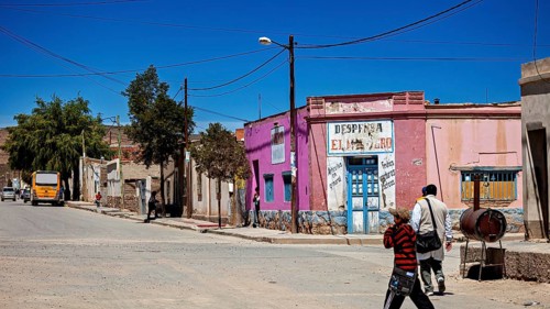 Colourful buildings and people in a bright, dry village with hills in the background, San Antonio